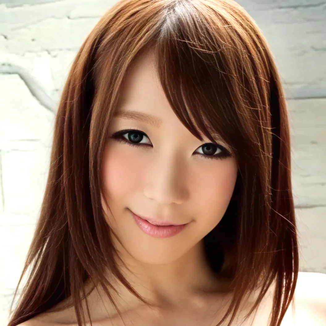 白い壁を背景に、こちらを向いて優しく微笑んでいる、茶髪でロングヘアーの女性、沖ひとみさん。