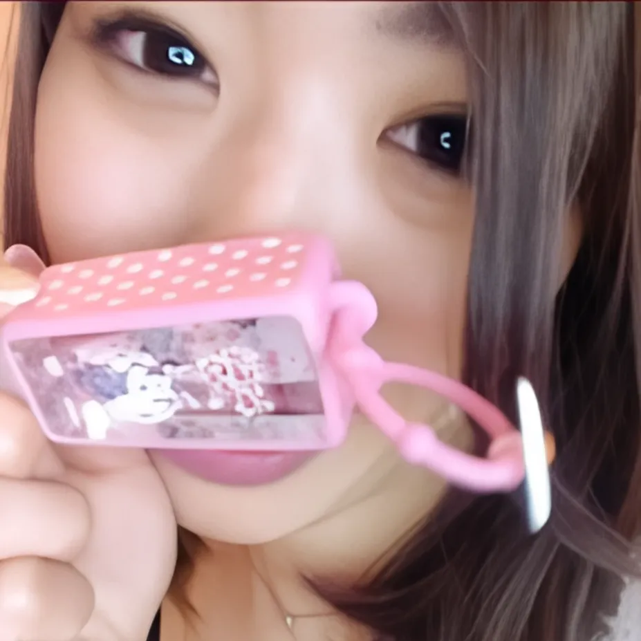 ピンク色のキャラクターキーホルダーを口元に持ってきて、こちらを見ている女性、りなさんのクローズアップ。